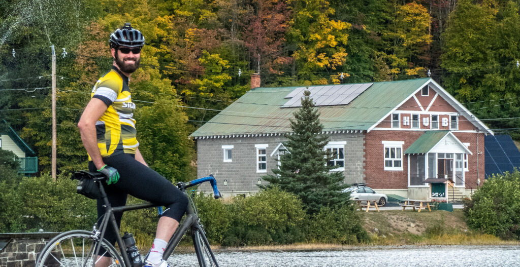 Guy on a bike smiling at the camera with a brick building in the background