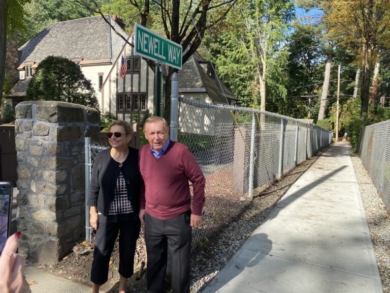 A man and a woman stand in front of the sign with the empty path behind them.