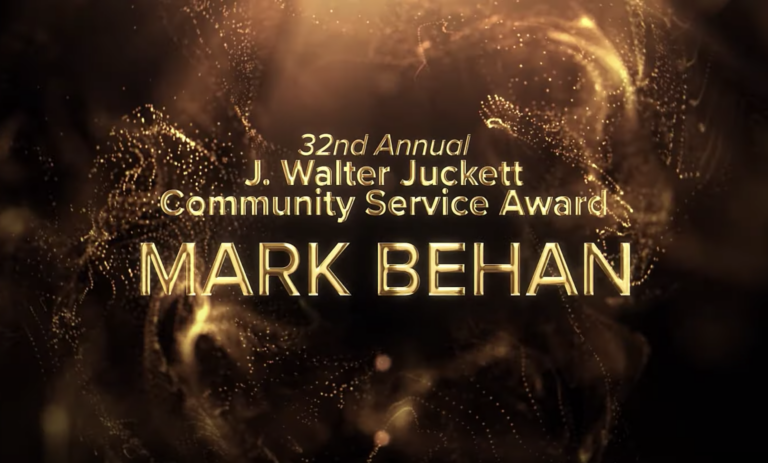 Gold lettering over a black and gold swirling background reads: 32nd Annual J. Walter Juckett Community Service Award Mark Behan.