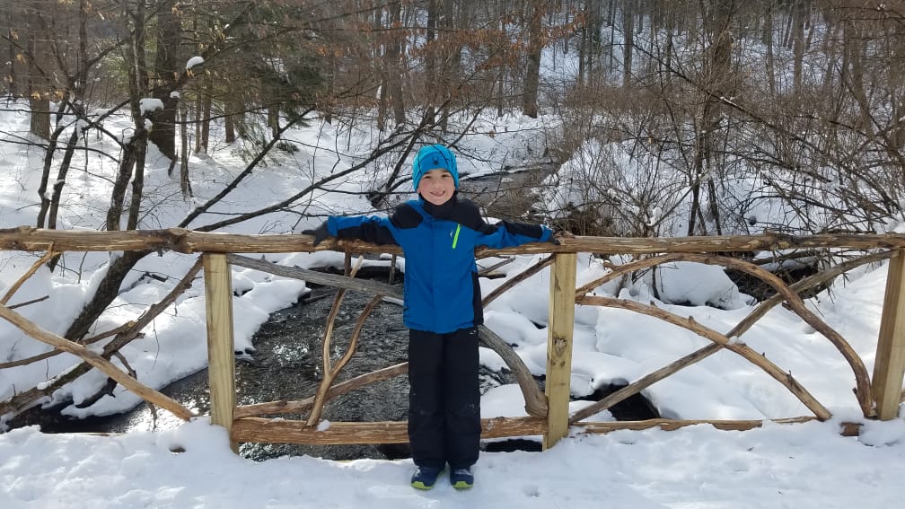 kid standing on a snowy bridge smiling at camera