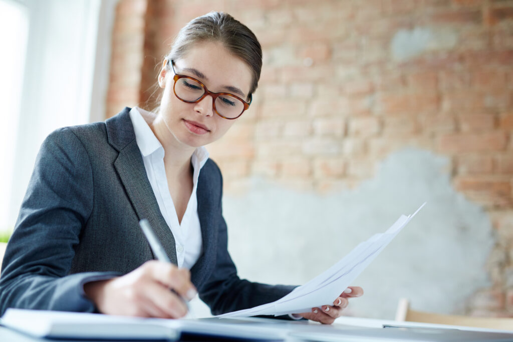 Woman in eyeglasses and suit writing down her working ideas in notebook