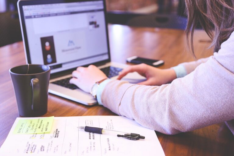 Woman's hands typing on a laptop with a cup of coffee nearby