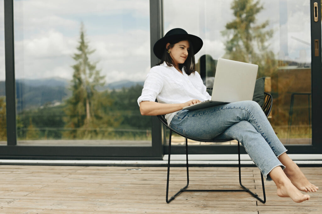 Woman on porch with laptop and reflection of mountains behind her