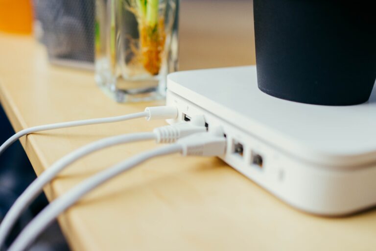 A white wireless router sits on a wooden table with white cords coming out of it